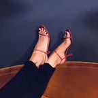 Sandália feminina vermelha nos pés com tiras delicadas e salto fino, estilo moderno e sofisticado.